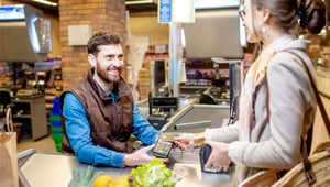 Supermarktangestellte an einer Kasse, die eine Kartenzahlung von einem Kunden entgegennimmt