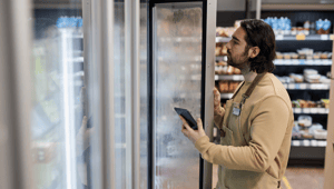 Männlicher Angestellter der mittels KI im Einzelhandel den Bestand in einer Supermarkt-Tiefkühltruhe mittles KI überprüft