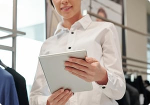 Luxury retail sales consultant in a stylish white button-down shirt, expertly utilizing a sleek silver tablet to access the tamigo workforce management app.