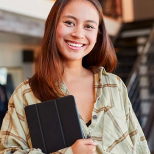Cheerful female sales assistant smiling warmly at the camera, confidently holding a tablet in her arm.
