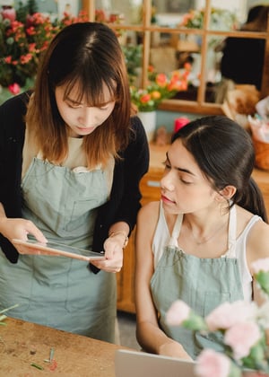 Betrokken vrouwelijke verkoopmedewerkers, stijlvol gekleed in groene schorten, werken samen om retailactiviteiten te optimaliseren met behulp van hun intuïtieve retailmanagement software op een tablet.