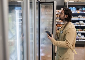 Um funcionário de uma supermercado olha para um frigorífico para verificar se os produtos alimentares disponíveis correspondem ao stock registado na aplicação.