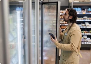 Un employé de l'épicerie regarde dans un réfrigérateur pour vérifier si les produits alimentaires disponibles correspondent au stock enregistré dans l'application